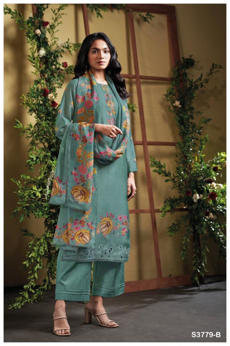 Woman wearing a teal embroidered outfit with a floral shawl in a decorated indoor setting.
