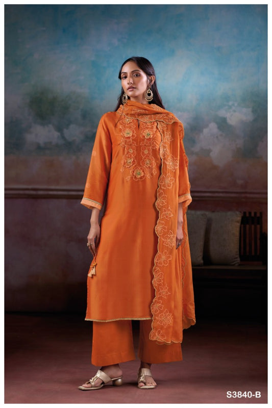 Woman wearing an orange traditional outfit with intricate patterns against a textured wall.