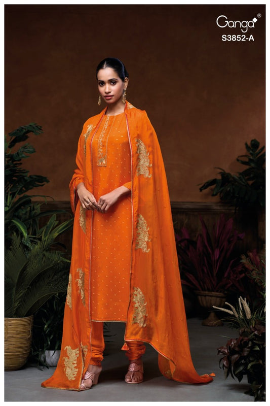 Woman wearing an orange traditional outfit with gold embroidery, standing against a brown background with plants.
