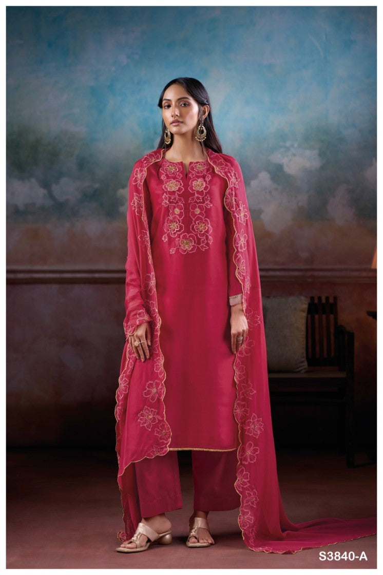Woman wearing a pink traditional outfit with intricate designs against a decorative wall.